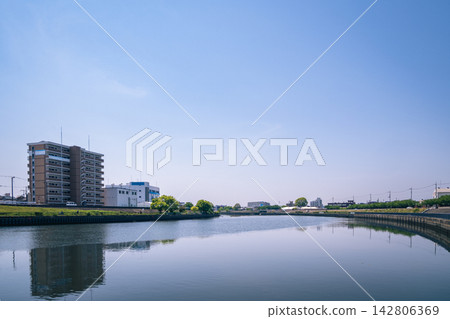 The blue sky and white apartment buildings are reflected on the calm surface of the river. 142806369