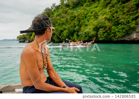 Boatman enjoying scenic longtail boat cruise in andaman sea Boatman enjoying scenic longtail boat cruise in andaman sea 142806585