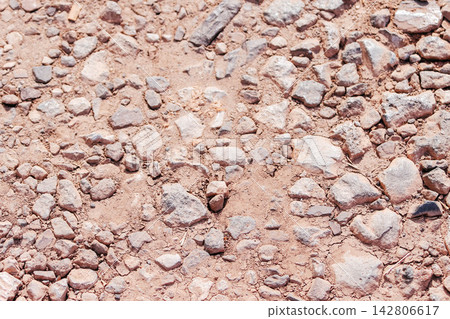 Top-down high-angle shot of dry, reddish soil and gravel ground texture with small scattered rocks. Ideal background for nature, environmental, drought, construction, and outdoor trail concepts. Top-down high-angle shot of dry, reddish soil and gravel ground texture with small scattered rocks. Ideal background for nature, environmental, drought, construction, and outdoor trail concepts. 142806617