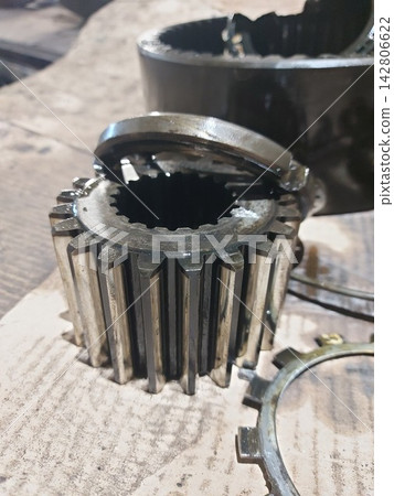 Close-up shot of a steel mechanical gear with splines and ring components during repair work on a workbench. Concept of industrial engineering, automotive repair, machine maintenance, and spare parts. Close-up shot of a steel mechanical gear with splines and ring components during repair work on a workbench. Concept of industrial engineering, automotive repair, machine maintenance, and spare parts. 142806622