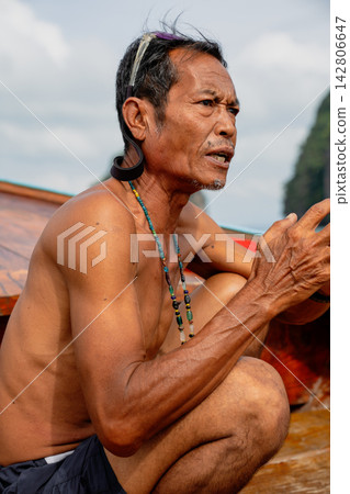 Older man squatting, talking, wearing necklace on boat Older man squatting, talking, wearing necklace on boat 142806647