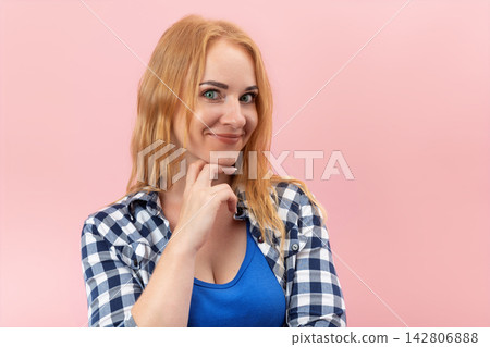 Young woman with red hair and blue eyes looking at the viewer with a clever smirk, her hand resting under chin, conveying a sense of intrigue, secret, or thoughtful consideration Young woman with red hair and blue eyes looking at the viewer with a clever smirk, her hand resting under chin, conveying a sense of intrigue, secret, or thoughtful consideration 142806888