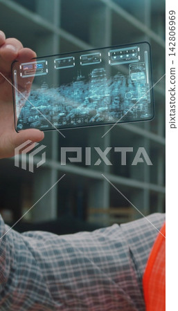 Vertical video. Close up Architect or Engineer using smartphone transparent hologram digital display application in front of building under construction. Technology, people. 142806969