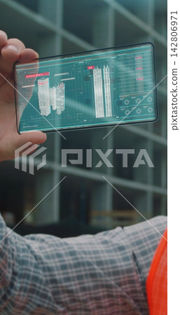 Vertical video. Close up Architect or Engineer using smartphone transparent hologram digital display application in front of building under construction. Technology, people. Vertical video. Close up Architect or Engineer using smartphone transparent hologram digital display application in front of building under construction. Technology, people. 142806971