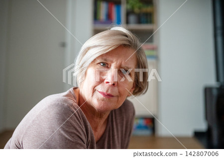 Smiling elderly woman looking through window at home. Smiling elderly woman looking through window at home. 142807006
