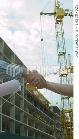 Vertical video. Close up Man architects engineers and male client shaking hands at construction site. Professions, construction, workers, architect concept. Vertical video. Close up Man architects engineers and male client shaking hands at construction site. Professions, construction, workers, architect concept. 142807025