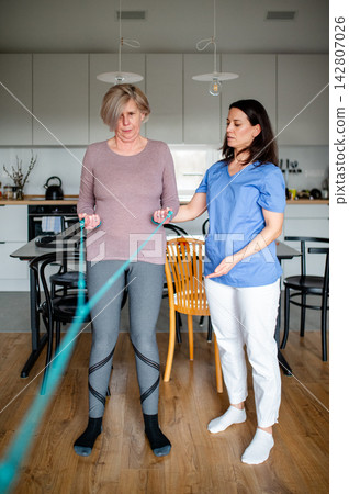 Physiotherapist guiding senior woman during resistance band exercise. Physiotherapist guiding senior woman during resistance band exercise. 142807026