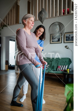 Physiotherapist guiding senior woman during resistance band exercise. Physiotherapist guiding senior woman during resistance band exercise. 142807027