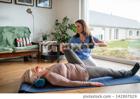 Physiotherapist exercising with senior woman on gym mat. Physiotherapist exercising with senior woman on gym mat. 142807029