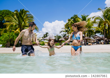 Happy family with daughter playing together in shallow tropical sea water during summer vacation. Happy family with daughter playing together in shallow tropical sea water during summer vacation. 142807061