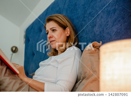 Nighttime routine for mature woman, reading book. Nighttime routine for mature woman, reading book. 142807091