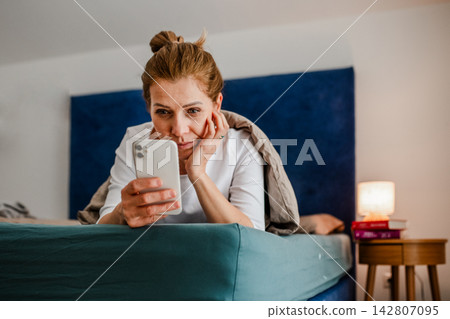 Woman lying under blanket and scrolling on phone. Woman lying under blanket and scrolling on phone. 142807095
