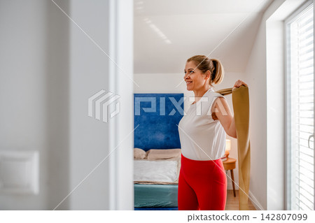 Smiling middle aged woman exercising with resistance band at home. Smiling middle aged woman exercising with resistance band at home. 142807099