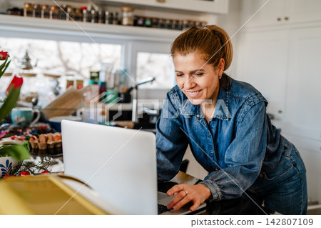 Mature woman searching recipe online on laptop while cooking in kitchen. 142807109