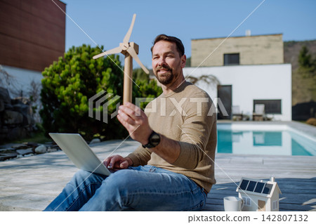 Man holding wind turbine model and laptop. Renewable energy concept. Man holding wind turbine model and laptop. Renewable energy concept. 142807132