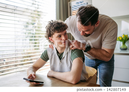 Father supporting teenage son at home during everyday moment. 142807149