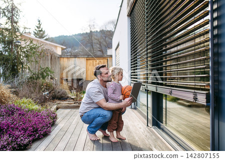 Father controlling smart home exterior blinds using tablet while standing with toddler son. Father controlling smart home exterior blinds using tablet while standing with toddler son. 142807155