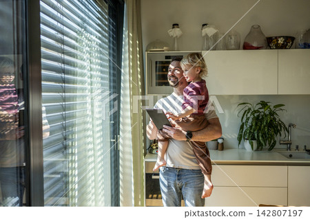 Father showing smart home control to toddler while managing exterior shading system. Father showing smart home control to toddler while managing exterior shading system. 142807197