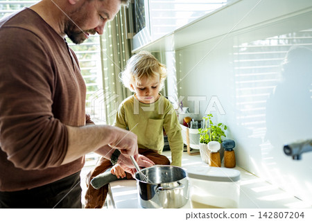 Dad and toddler preparing simple meal together in bright kitchen. Dad and toddler preparing simple meal together in bright kitchen. 142807204