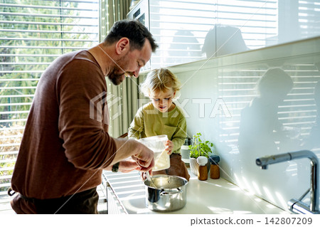 Dad and toddler preparing simple meal together in bright kitchen. Dad and toddler preparing simple meal together in bright kitchen. 142807209