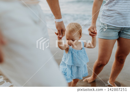Parents holding hands with little toddler girl, walking on beach during beach holiday. Parents holding hands with little toddler girl, walking on beach during beach holiday. 142807251