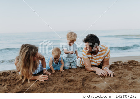 Two toddler children playing on sand beach with paretns during summer holiday. Two toddler children playing on sand beach with paretns during summer holiday. 142807252
