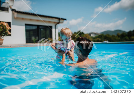 Father and young daughter playing in pool. Father and young daughter playing in pool. 142807270