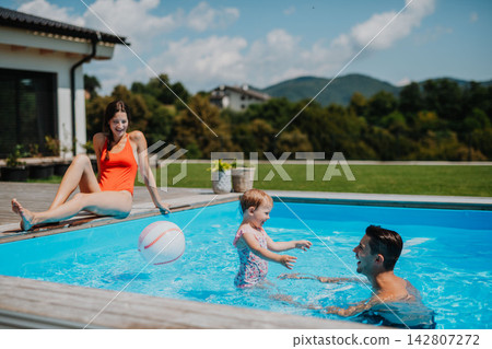 Young family with small daughter in swimming pool outdoors in backyard garden. Young family with small daughter in swimming pool outdoors in backyard garden. 142807272