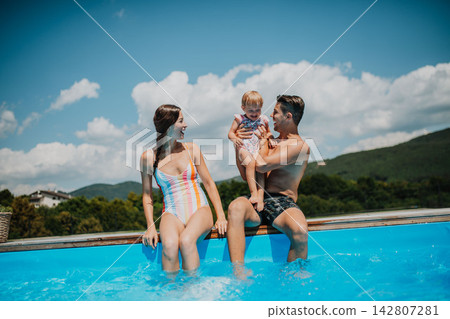 Young family with small daughter in swimming pool outdoors in backyard garden. Young family with small daughter in swimming pool outdoors in backyard garden. 142807281