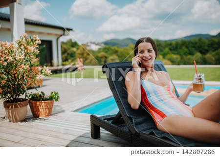 Young woman in swimsuit sitting by pool, making phone call. Young woman in swimsuit sitting by pool, making phone call. 142807286