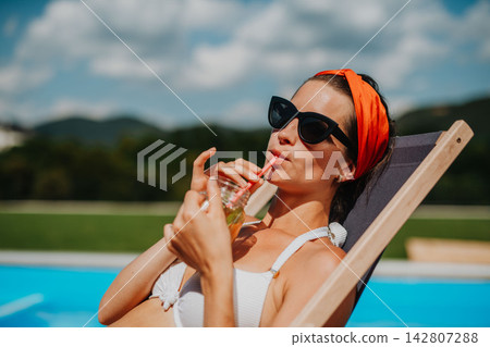 Young woman sitting by swimming pool and drinking limonade. Young woman sitting by swimming pool and drinking limonade. 142807288