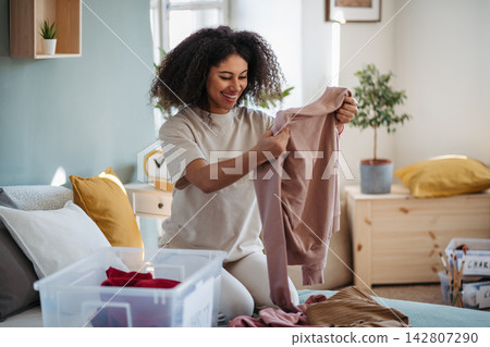 Young woman sorting wardrobe indoors at home, charity donation concept. Young woman sorting wardrobe indoors at home, charity donation concept. 142807290