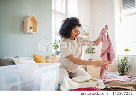 Young woman sorting wardrobe indoors at home, charity donation concept. Young woman sorting wardrobe indoors at home, charity donation concept. 142807291