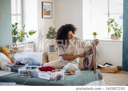Young woman sorting wardrobe indoors at home, charity donation concept. Young woman sorting wardrobe indoors at home, charity donation concept. 142807293