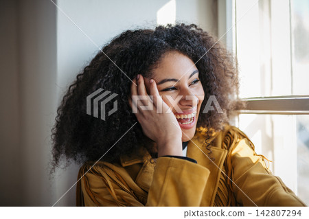 Portrait of beautiful young woman sitting on window sill. Portrait of beautiful young woman sitting on window sill. 142807294