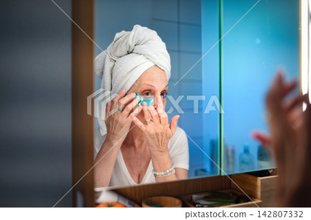 Senior woman applying skincare product during morning beauty routine at home. Senior woman applying skincare product during morning beauty routine at home. 142807332
