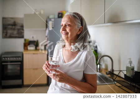 Senior woman starting her day with glass of fresh water at home. 142807333
