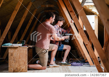Father teaching teenage son DIY skills while renovating attic together. Father teaching teenage son DIY skills while renovating attic together. 142807367