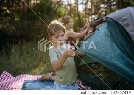 Girl and mom setting up tent together during summer camping trip. Girl and mom setting up tent together during summer camping trip. 142807419