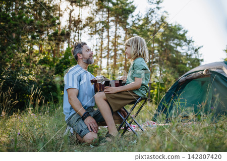 Dad teaching boy how to play guitar during summer camping adventure in nature. Dad teaching boy how to play guitar during summer camping adventure in nature. 142807420
