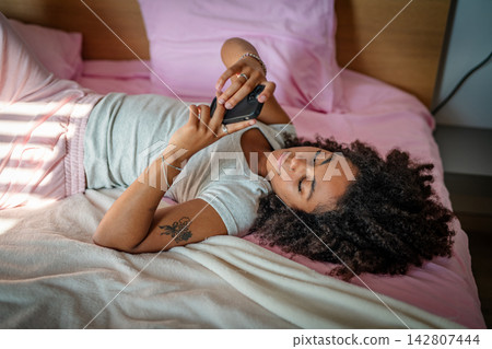 Young woman scrolling on smartphone while lying in bed. Young woman scrolling on smartphone while lying in bed. 142807444