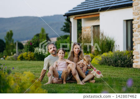 Family enjoying late summer evening together at their new house, sitting on grass. Family enjoying late summer evening together at their new house, sitting on grass. 142807462