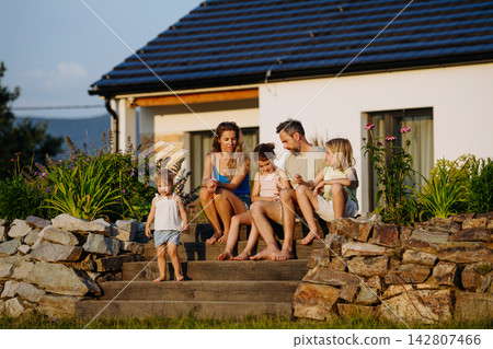 Happy young family spending summer evening together outside their new home. 142807466
