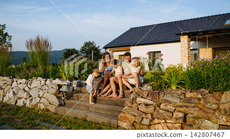 Happy young family spending summer evening together outside their new home. Happy young family spending summer evening together outside their new home. 142807467