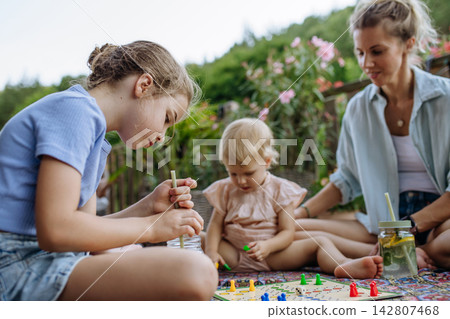 Family enjoying board game together on outdoor terrace during summer. Family enjoying board game together on outdoor terrace during summer. 142807468