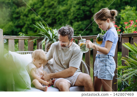 Father enjoying summer drinks with his daughters on outdoor terrace. Father enjoying summer drinks with his daughters on outdoor terrace. 142807469