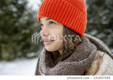 Smiling teenage girl standing outdoors in falling snow. Smiling teenage girl standing outdoors in falling snow. 142807488