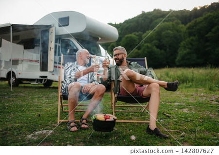 Father and adult son grilling beside camper during family RV vacation. Father and adult son grilling beside camper during family RV vacation. 142807627
