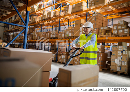 Senior woman working in warehouse, wearing reflective vest. 142807700