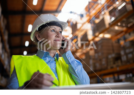 Female warehouse manager or supervisor with smartphone, making phone call. Female warehouse manager or supervisor with smartphone, making phone call. 142807723